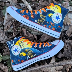 May include: A pair of black and blue high-top sneakers with orange laces. The sneakers are decorated with a Jack Skellington design from the movie "The Nightmare Before Christmas". The text "WAHRE LIEBIE STIRBT ONIE O" is printed on the side of the sneakers.