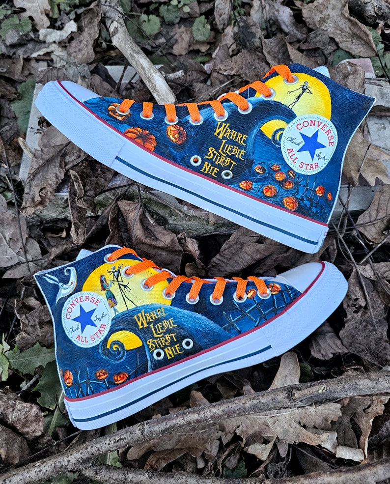 May include: A pair of black and blue high-top sneakers with orange laces. The sneakers are decorated with a Jack Skellington design from the movie "The Nightmare Before Christmas". The text "WAHRE LIEBIE STIRBT ONIE O" is printed on the side of the sneakers.