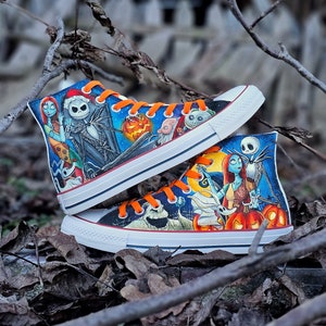 May include: A pair of high-top sneakers with a custom design featuring characters from the movie "The Nightmare Before Christmas". The sneakers are white with black and orange accents. The design includes Jack Skellington, Sally, and other characters from the film.