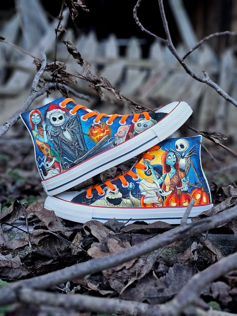 May include: A pair of high-top sneakers with a custom design featuring characters from the movie "The Nightmare Before Christmas". The sneakers are white with black and orange accents. The design includes Jack Skellington, Sally, and other characters from the film.