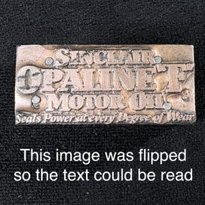 May include: A rectangular metal printing block with the text "SINCLAIR OPALINE F MOTOR OIL" and "Seals Power at every Degree of Wear". The block is silver-colored with raised lettering and is set against a dark background.