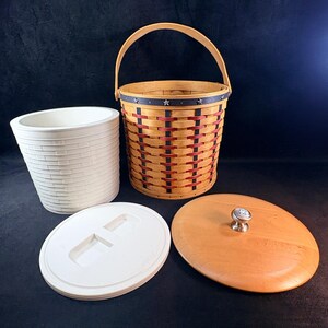 May include: A round woven basket with a swing handle, featuring a dark blue rim with small silver stars and alternating red and black vertical accents. The set includes a white plastic cylindrical liner, a white plastic lid, and a round wooden lid.