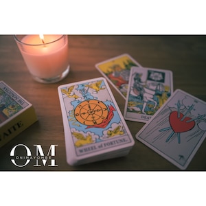 May include: A tarot card reading spread with a lit candle, a deck of tarot cards, and four cards laid out on a wooden table. The cards are "The Magician", "Wheel of Fortune", "Death", and "Three of Swords".
