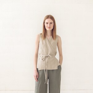 May include: A woman wearing a beige linen wrap top with a matching tie belt and olive green linen wide-leg pants. She is standing on a white wood floor.