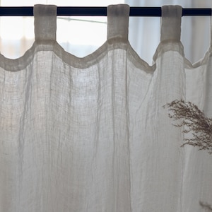 May include: White linen curtains with a gathered top and a rod hanging from the top. The curtains are sheer and allow light to pass through.