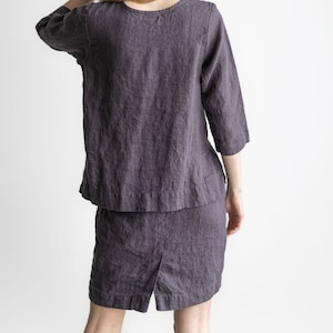 Op de afbeelding: Een vrouw draagt een donkergrijze linnen top en bijpassende shorts. De top heeft een ronde hals en 3/4 mouwen. De shorts hebben een rechte pijp en komen tot halverwege de dij.