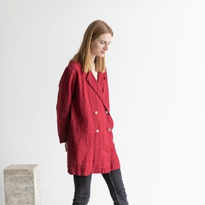 Può includere: Una donna indossa un blazer di lino rosso con chiusura a doppio petto e jeans neri. È in piedi su una piattaforma di cemento e indossa stivali neri con lacci.