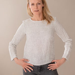 May include: A long-sleeved top featuring a white base with thin, horizontal black stripes, a round neckline, and a straight hemline, paired with dark gray denim jeans. The garment has a textured fabric appearance and a fitted silhouette.
