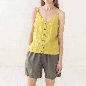 May include: A woman wearing a yellow linen tank top with a button-down front and matching olive green linen shorts.