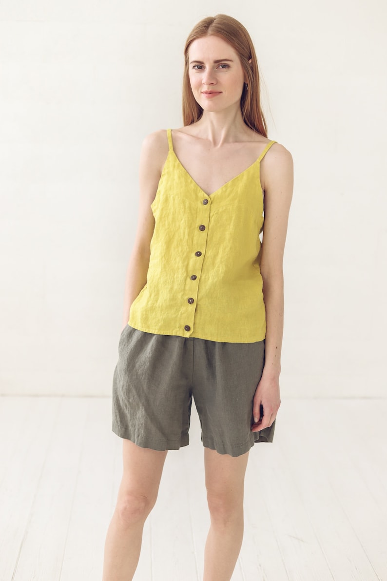 May include: A woman wearing a yellow linen tank top with a button-down front and matching olive green linen shorts.