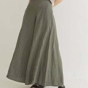 May include: A woman is wearing a pair of wide-leg, olive green linen pants. The pants have a high waist and a flowing silhouette. She is wearing brown sandals.