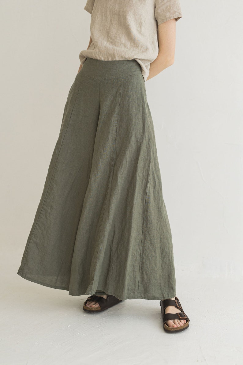 May include: A woman is wearing a pair of wide-leg, olive green linen pants. The pants have a high waist and a flowing silhouette. She is wearing brown sandals.