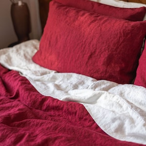 May include: A red and white linen bedding set with a textured, crinkled look. The bedding is arranged on a bed with a brown headboard.