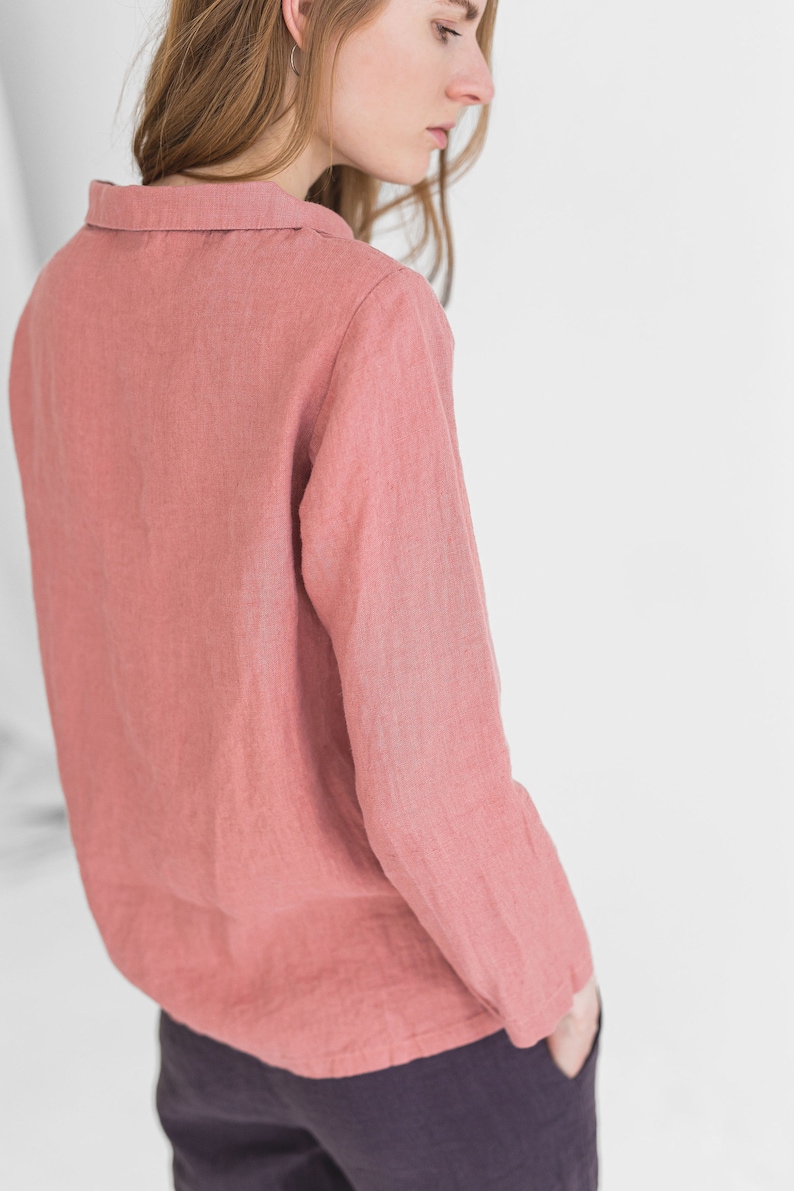 May include: A long-sleeved, collared shirt in a dusty rose colour. The shirt is made of a soft, textured fabric and has a relaxed fit.