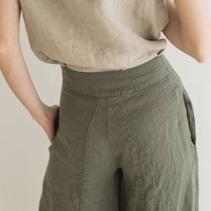 May include: A pair of wide-leg linen pants in a dark olive green color. The pants have a high waist and a relaxed fit. The fabric is lightweight and has a subtle texture.