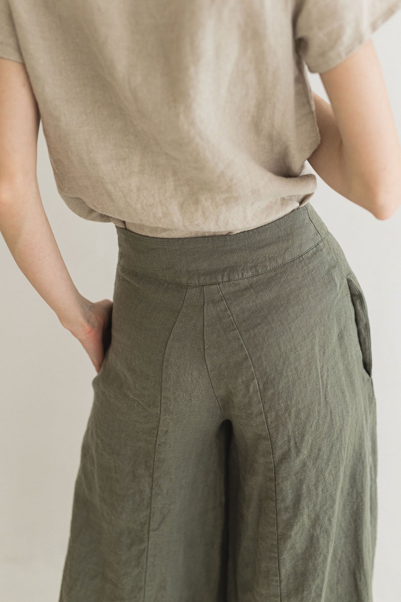 May include: A pair of wide-leg linen pants in a dark olive green color. The pants have a high waist and a relaxed fit. The fabric is lightweight and has a subtle texture.