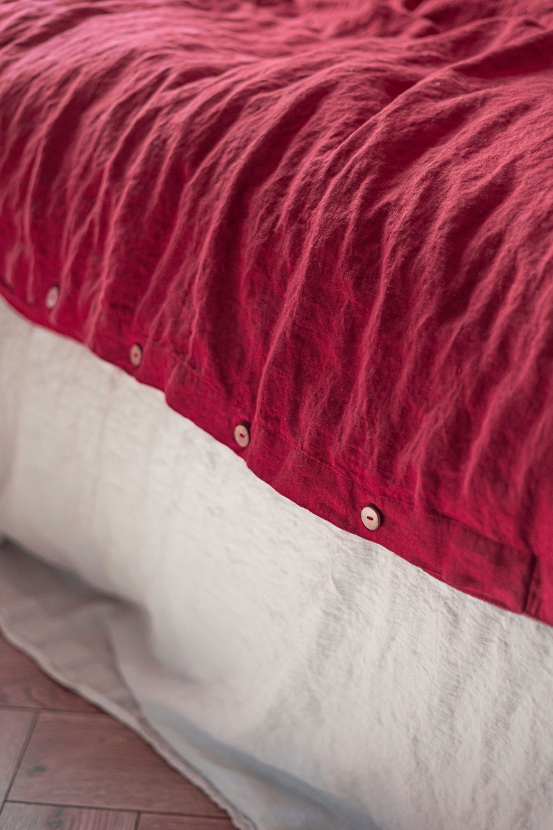 May include: A red linen duvet cover with wooden buttons. The duvet cover is folded over a white linen sheet.