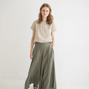 May include: A woman wearing a light beige linen top and wide-legged, olive green linen pants. She is wearing brown sandals.