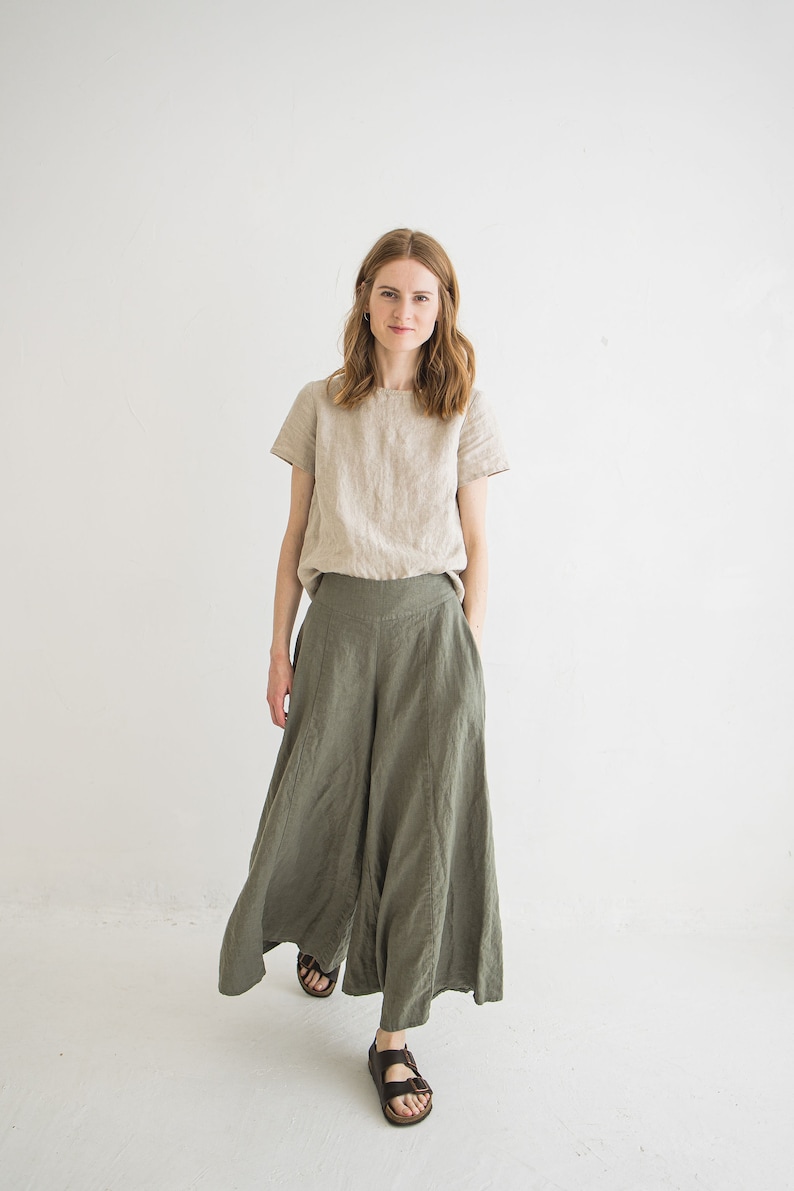May include: A woman wearing a light beige linen top and wide-legged, olive green linen pants. She is wearing brown sandals.