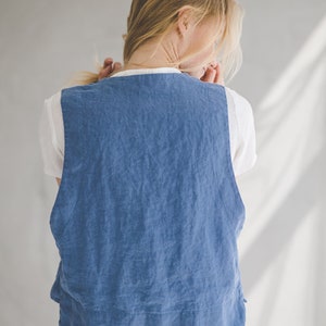 May include: A woman wearing a blue linen vest over a white t-shirt. The vest has a relaxed fit and a slightly cropped length. The woman is wearing blue denim pants.