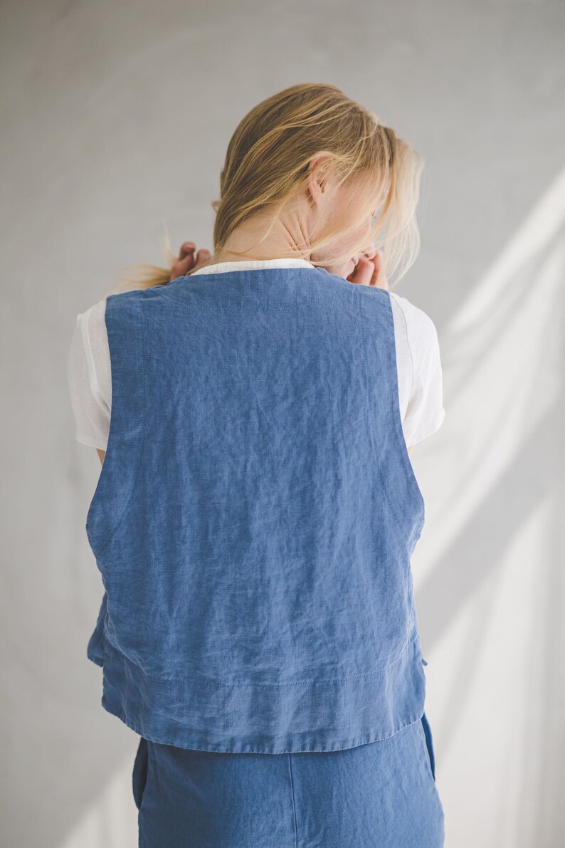 May include: A woman wearing a blue linen vest over a white t-shirt. The vest has a relaxed fit and a slightly cropped length. The woman is wearing blue denim pants.