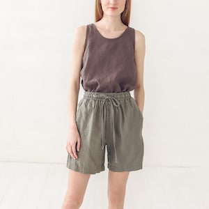 May include: A woman wearing a brown linen tank top and olive green linen shorts with a drawstring waist.