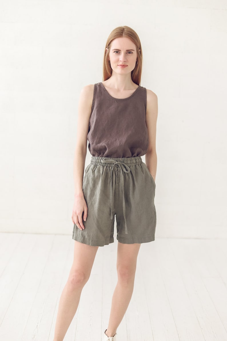 May include: A woman wearing a brown linen tank top and olive green linen shorts with a drawstring waist.