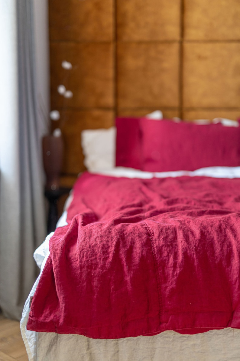 May include: A red linen duvet cover with a white linen bed skirt. The duvet cover is rumpled and has a relaxed, casual look.
