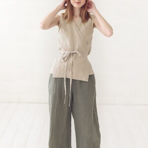 May include: A woman wearing a beige linen wrap top with a tie waist and olive green linen wide-leg pants.