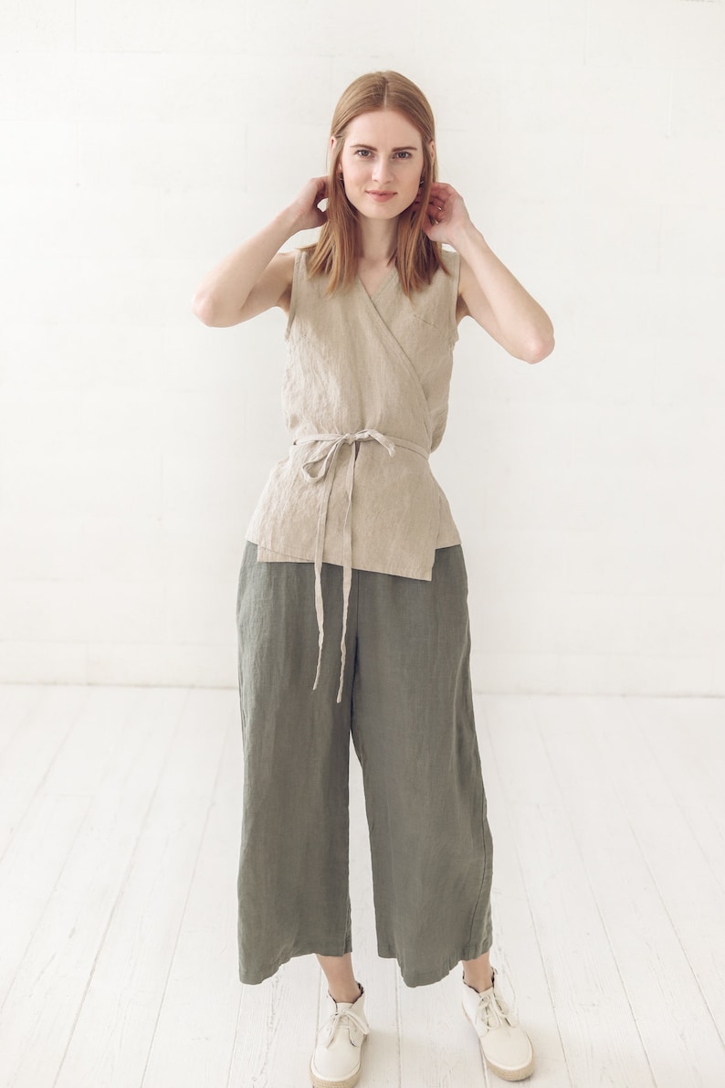 May include: A woman wearing a beige linen wrap top with a tie waist and olive green linen wide-leg pants.