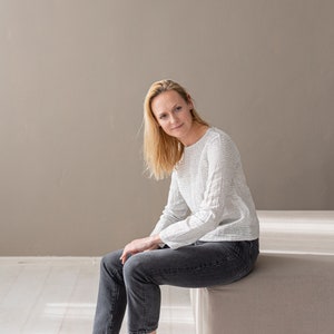 May include: A long-sleeved top featuring a white and black horizontal pinstripe pattern, paired with dark gray denim jeans and black low-top sneakers with white laces and white rubber soles. The top has a round neckline and a straight hemline.