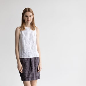 May include: A woman wearing a white linen tank top and a dark gray linen skirt.