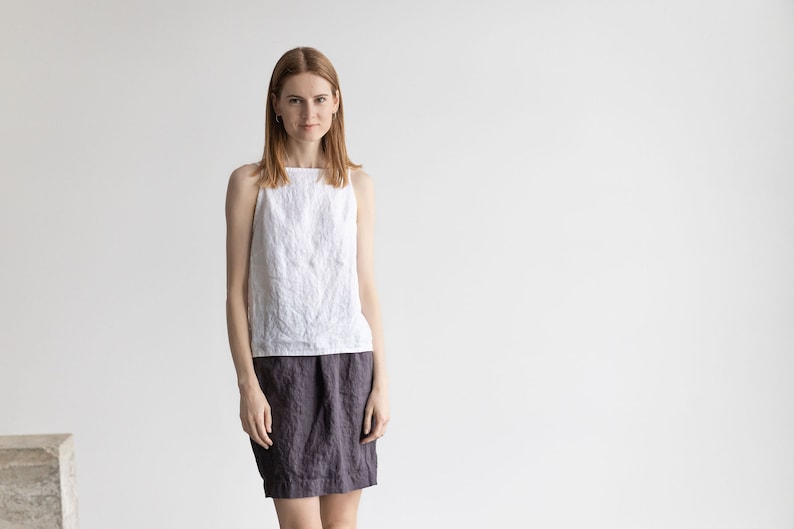 May include: A woman wearing a white linen tank top and a dark gray linen skirt.