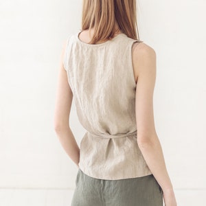 May include: A woman wearing a beige linen sleeveless top with a tie at the waist and olive green linen pants.