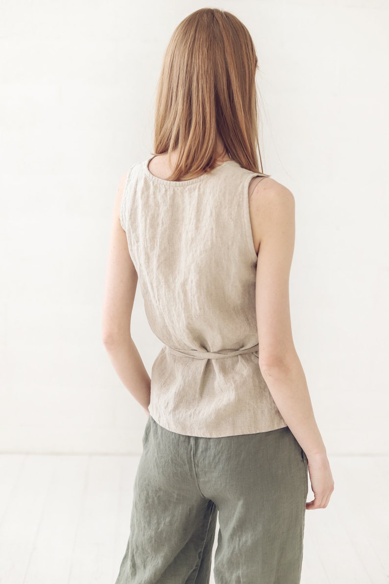 May include: A woman wearing a beige linen sleeveless top with a tie at the waist and olive green linen pants.