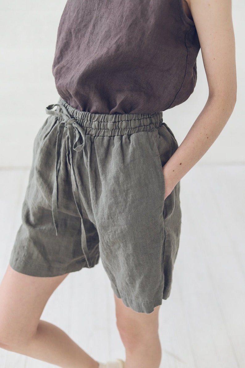 May include: A pair of olive green linen shorts with a drawstring waist and pockets. The shorts are made of a lightweight, breathable fabric and are perfect for warm weather.