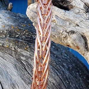 Könnte beinhalten: Ein Armband aus Kupferdraht mit geflochtenem Design. Das Armband ist hellkupferfarben und hat eine glänzende Oberfläche.