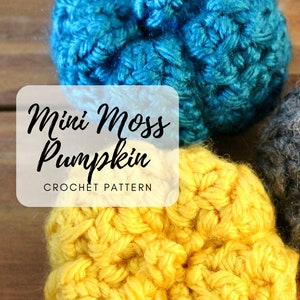 May include: Close-up of three crocheted mini pumpkins in shades of blue, yellow, and gray. The text "Mini Moss Pumpkin Crochet Pattern" is overlaid on the image. The pumpkins are made with a textured stitch.