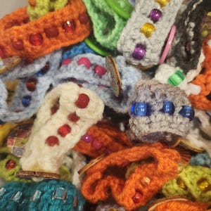 May include: A close-up of a pile of colorful crocheted bracelets with beads. The bracelets are made with different colored yarns and feature various beads, including colorful glass beads and wooden beads.