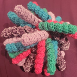 May include: A crocheted ball of yarn in shades of pink, purple, teal, and green. The yarn is arranged in a spiral pattern, creating a unique and colourful texture.