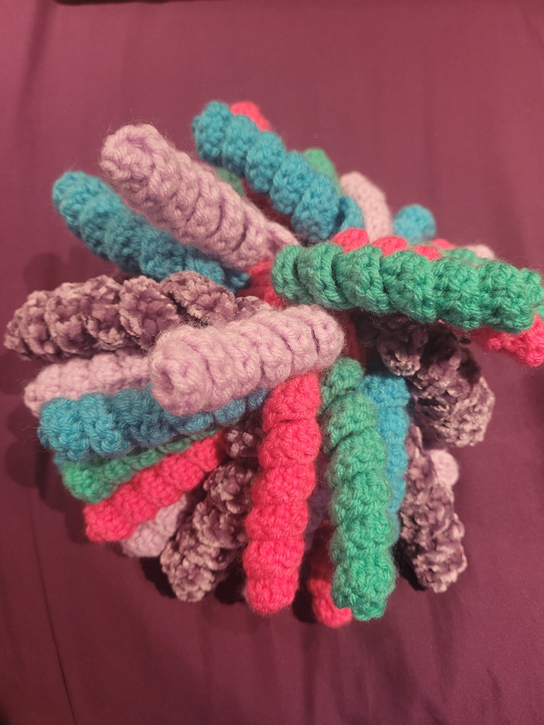 May include: A crocheted ball of yarn in shades of pink, purple, teal, and green. The yarn is arranged in a spiral pattern, creating a unique and colourful texture.