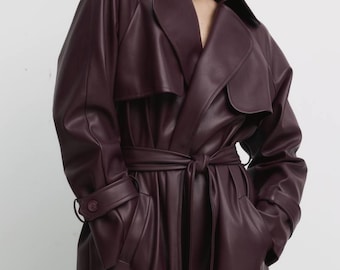 May include: A long, burgundy faux leather trench coat with a belt and pockets.