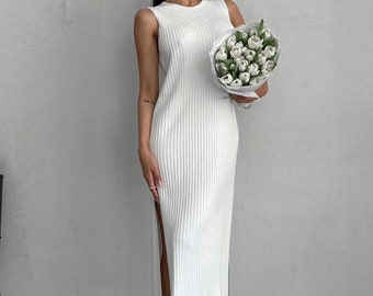 May include: A white sleeveless midi dress with a ribbed texture and a side slit. The dress is shown on a model holding a bouquet of white flowers.