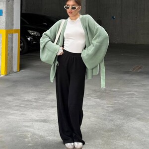 Puede incluir: Una mujer con un c&aacute;rdigan verde claro de manga larga y una camisa blanca. Lleva pantalones negros y zapatillas blancas.