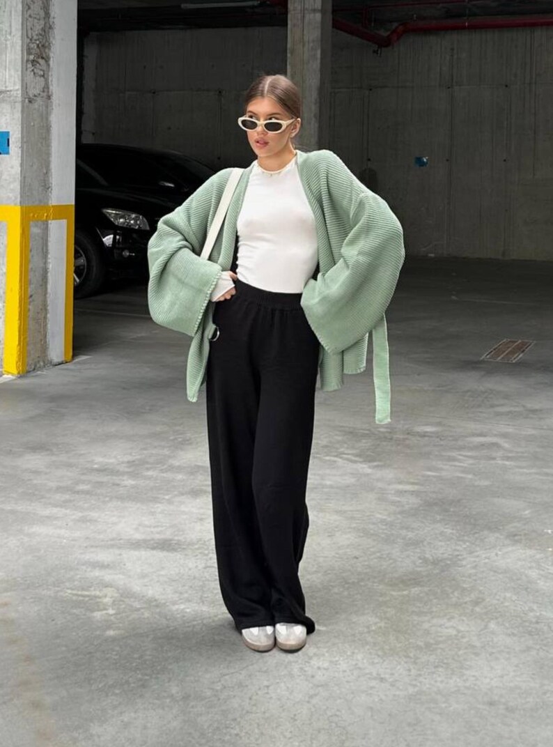 Puede incluir: Una mujer con un c&aacute;rdigan verde claro de manga larga y una camisa blanca. Lleva pantalones negros y zapatillas blancas.