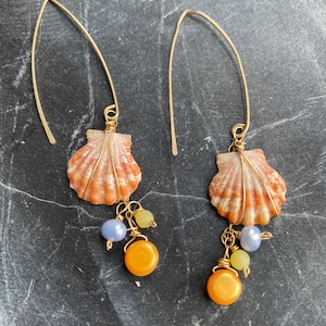 May include: A pair of gold dangle earrings featuring a seashell charm with orange, yellow, and blue glass beads.