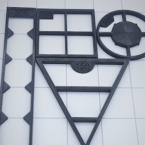 May include: A set of four black plastic stencils for crafting. The stencils include a rectangle with a grid pattern, a circle with a centre circle, a triangle with three lines, and a long rectangle with a series of triangles. The stencils are labelled with the measurements 30cm, 10cm, 10cm, and 15cm.