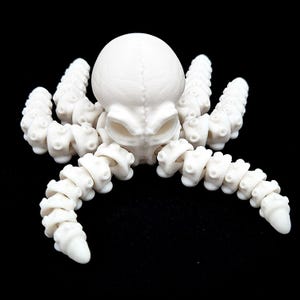 May include: A white, articulated octopus sculpture with a skull-like head and segmented tentacles. The sculpture is made of a smooth, matte material and is set against a black background. The octopus has a unique, skeletal appearance.