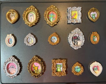 May include: A collection of fourteen miniature framed artworks featuring various colorful creature illustrations. The frames are ornate, metallic-toned in gold and silver, and come in diverse shapes including oval, rectangular, and heart-shaped designs.