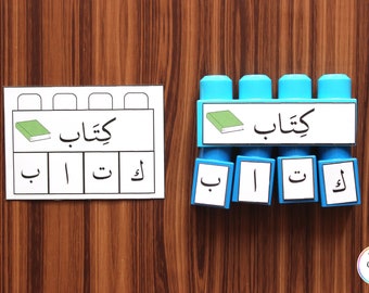May include: A blue and white learning tool with the Arabic word "kitab" (book) and the letters "b", "a", "t", and "k" on it. The word "kitab" is also written on a separate card with a picture of a book.